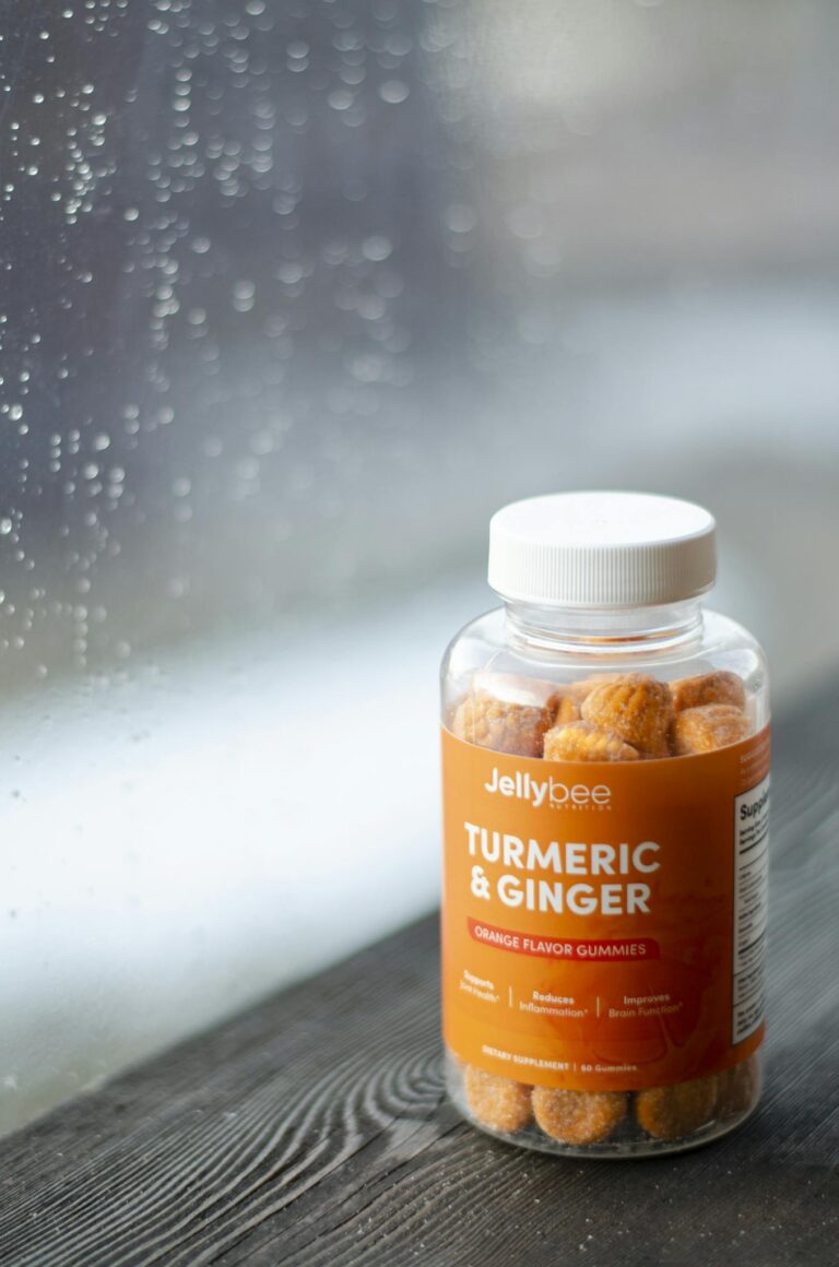 A bottle of Jellybee Turmeric & Ginger gummies sits on a wooden sill by a rainy window.
