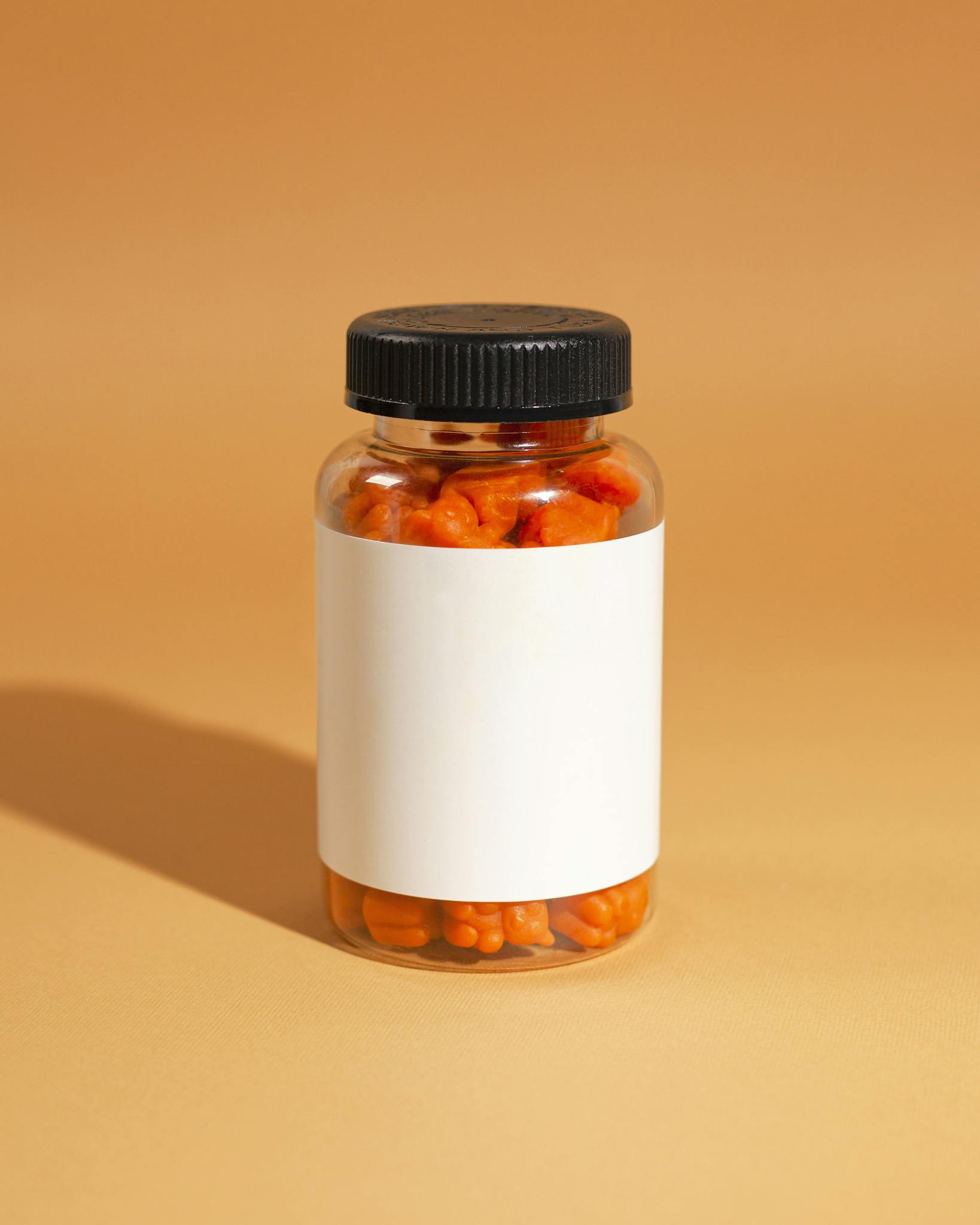 A clear bottle filled with orange gummy vitamins against an orange background.