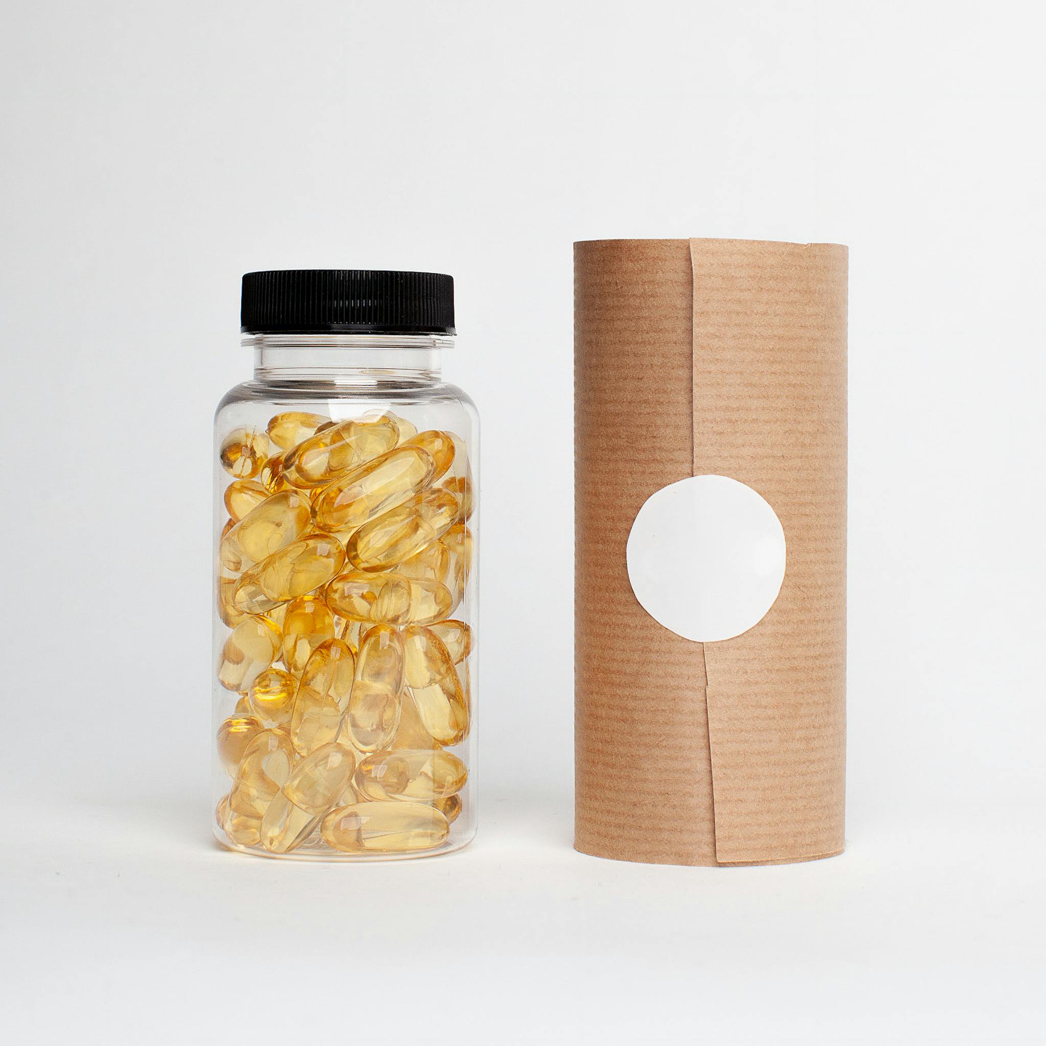 Clear plastic bottle filled with golden capsules next to a cardboard package on a white background.